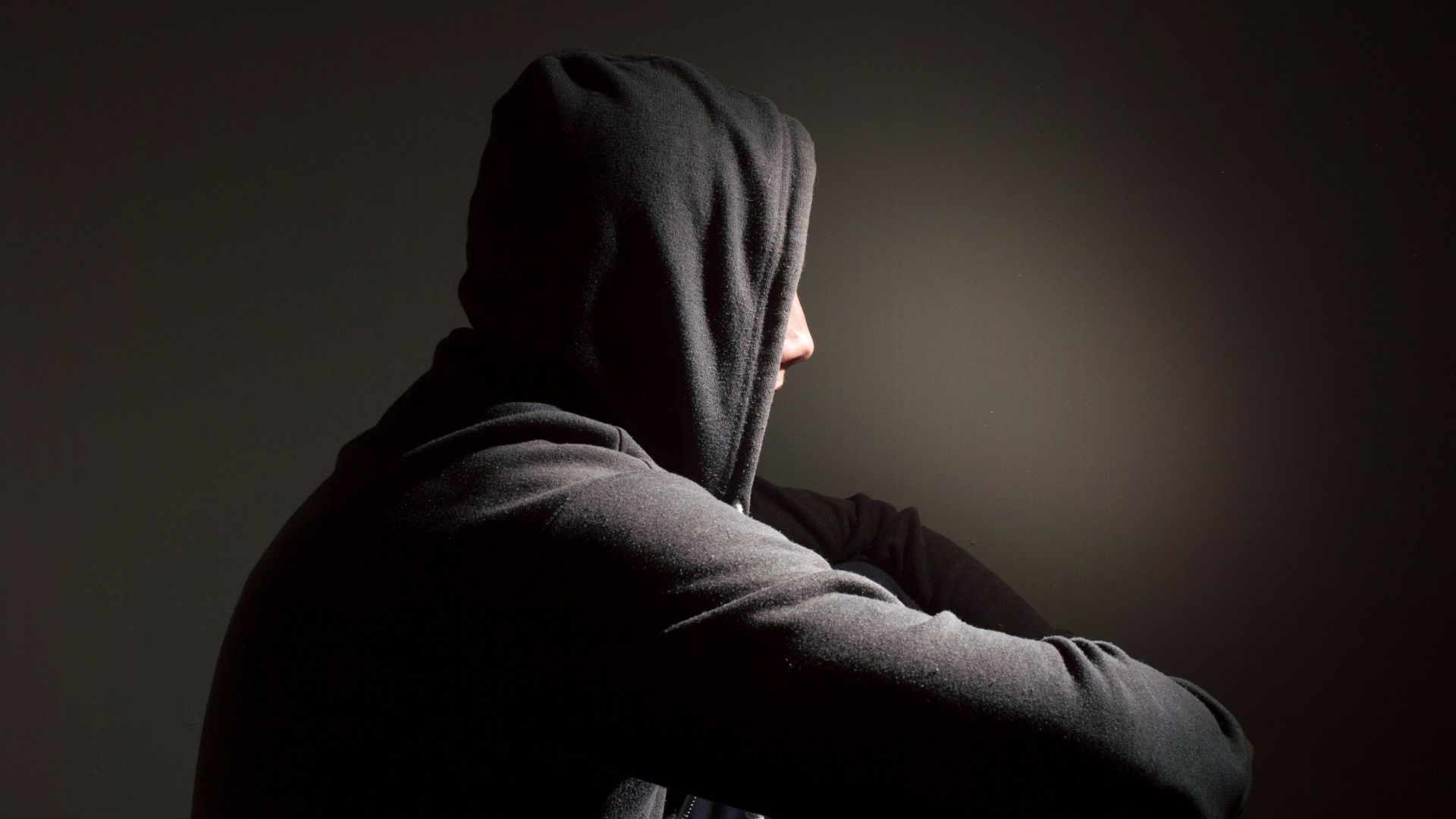 Teenager in black hoodie sitting and looking away from the camera