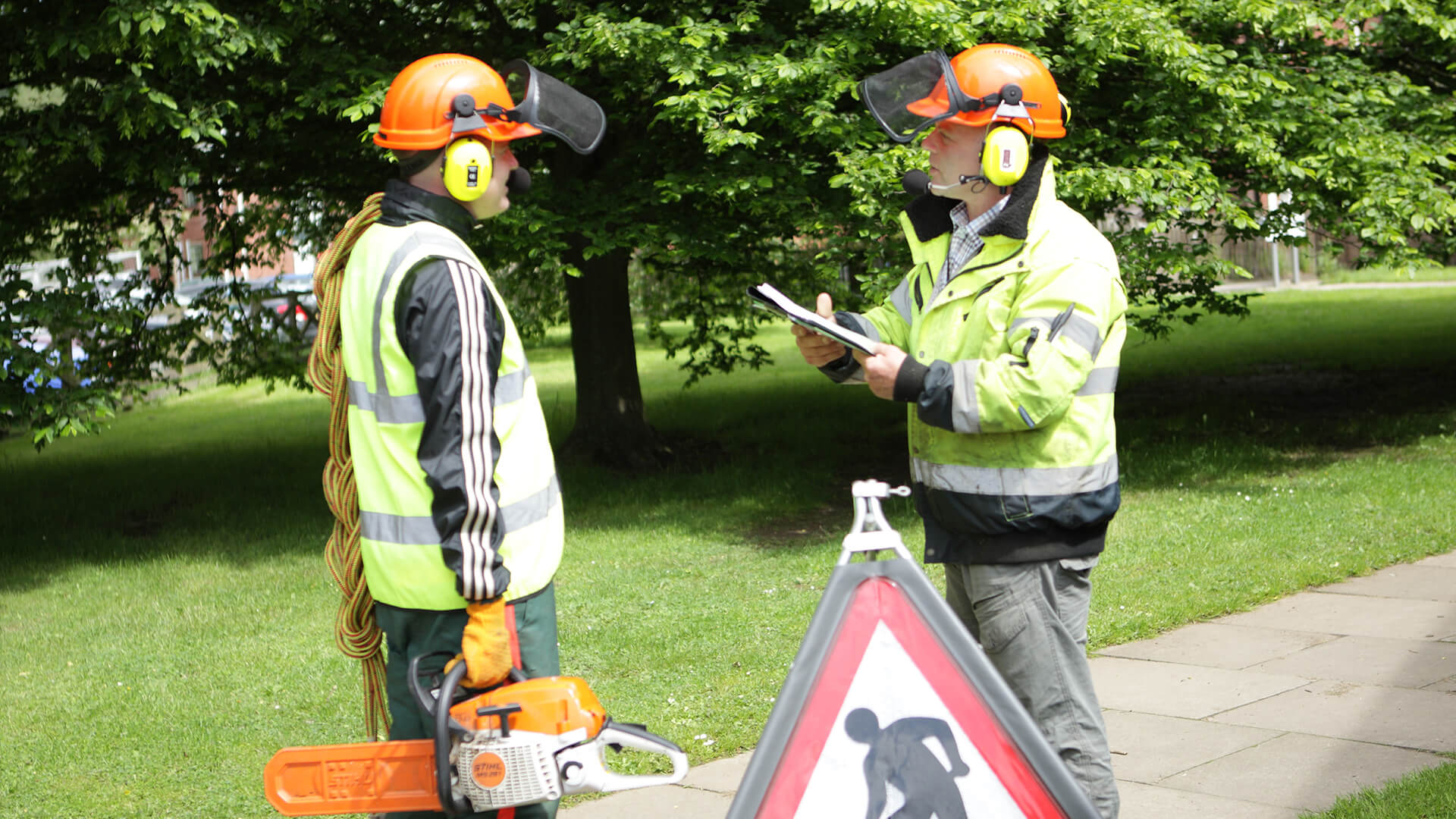 Two men wearing safety hard hat, goggles and high-vis jackets, having a conversation.