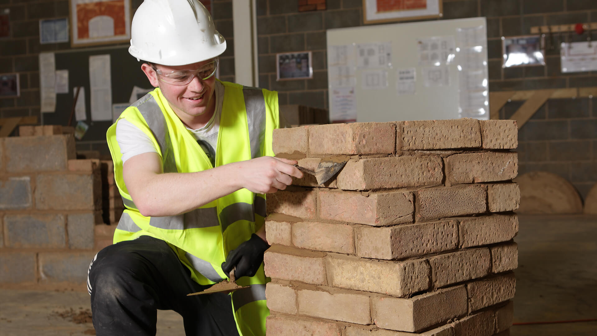 Young man wearing a hard hat and high-vis jacket, working on a stack of bricks.