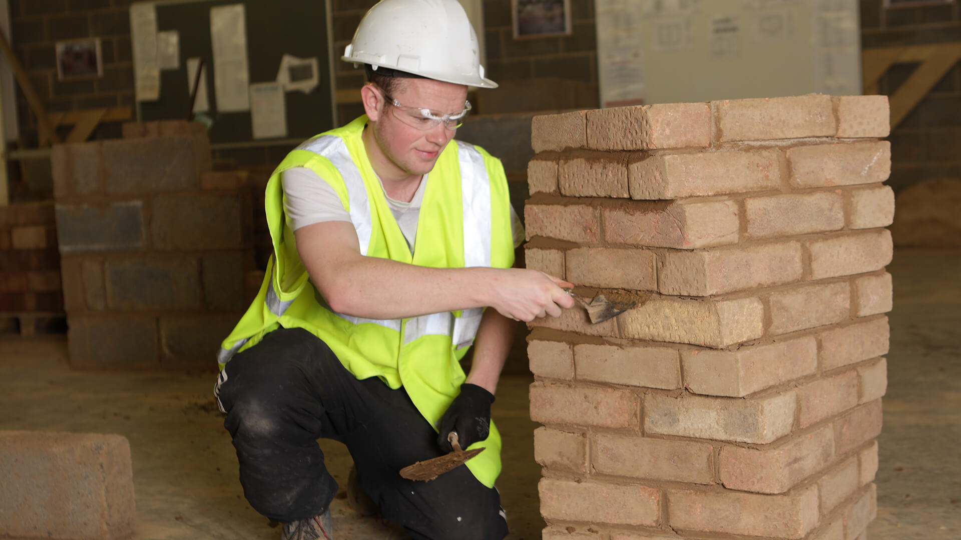 Young man crouching by a pile of bricks and working on them.