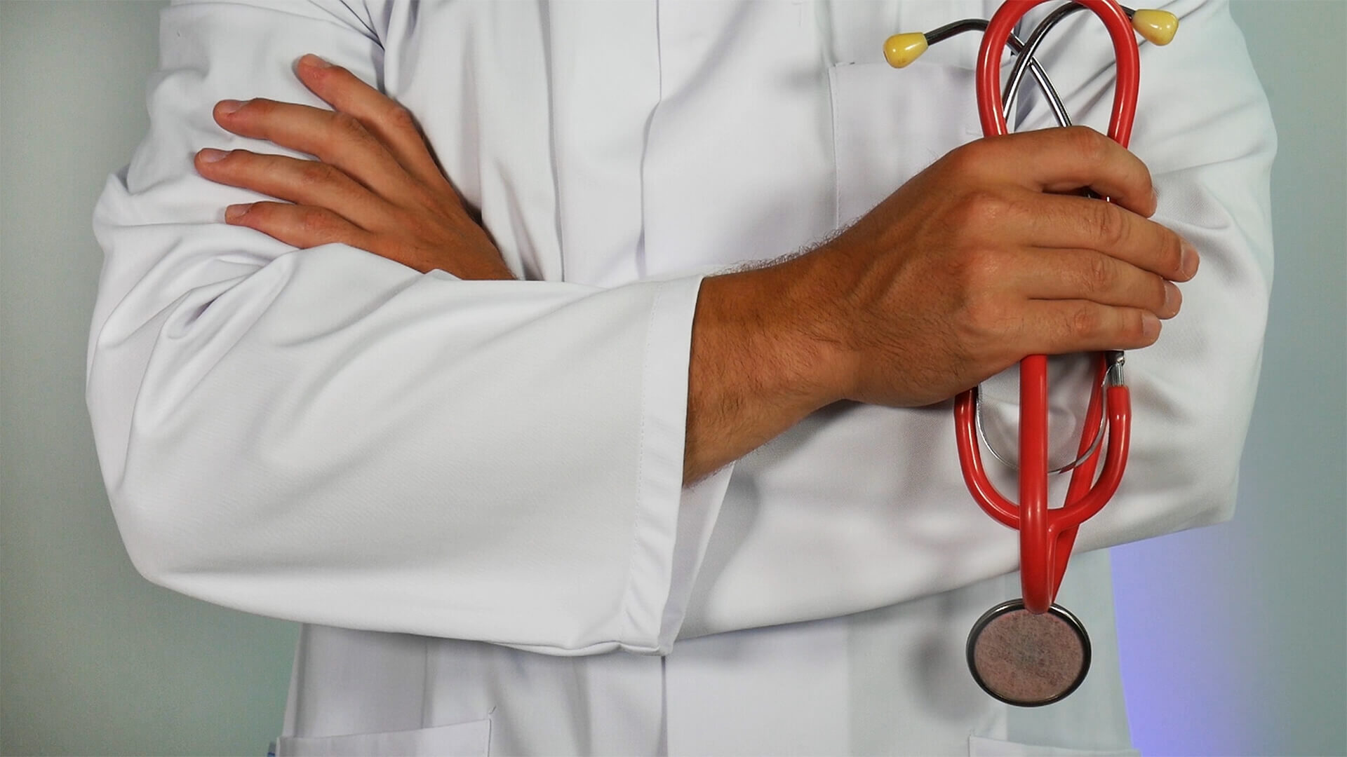 Man wearing a white lab coat and holding a stethoscope with his arms crossed.