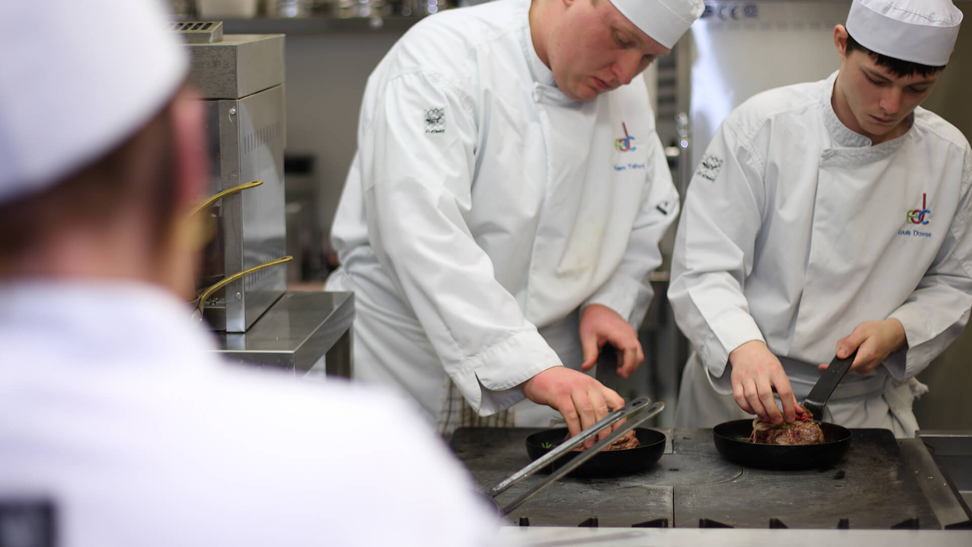 Three young chefs in chef uniforms working in a kitchen.