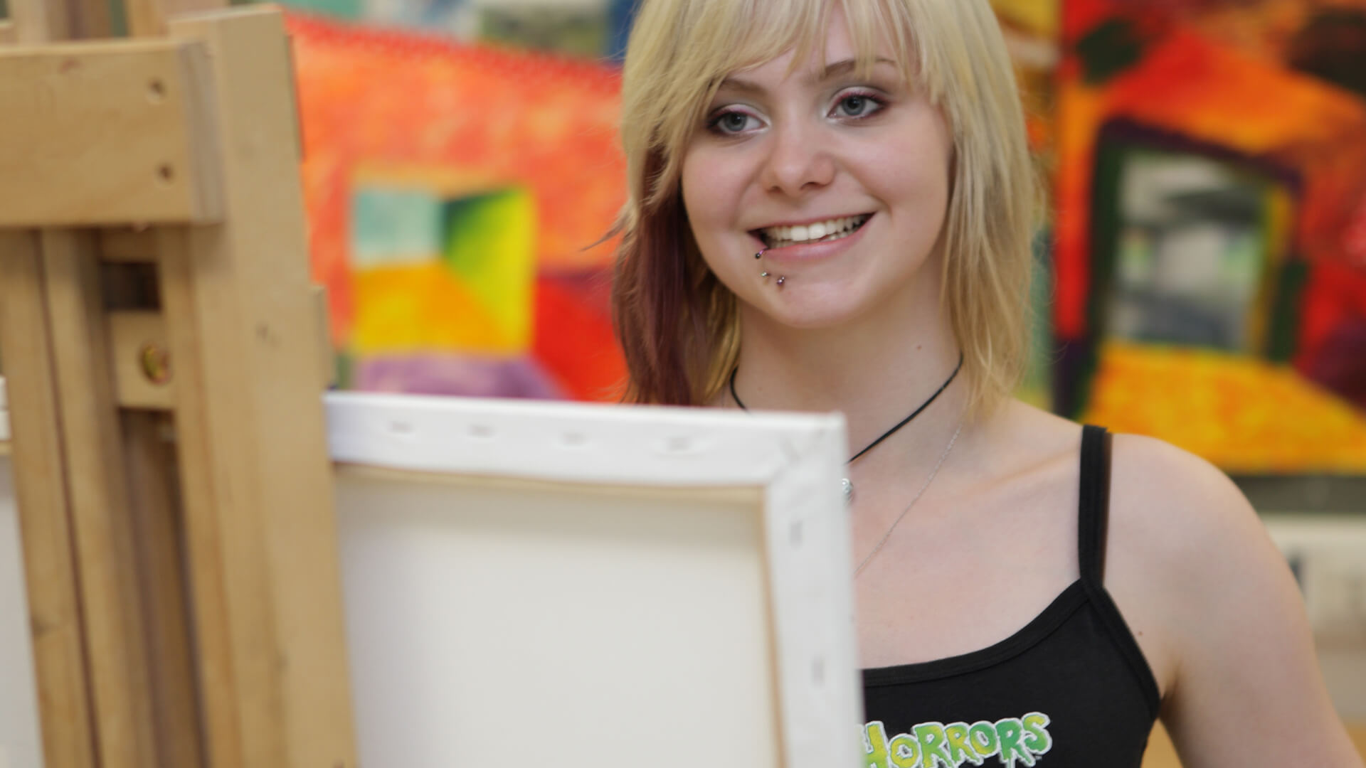 Young woman standing beside an easel and smiling.