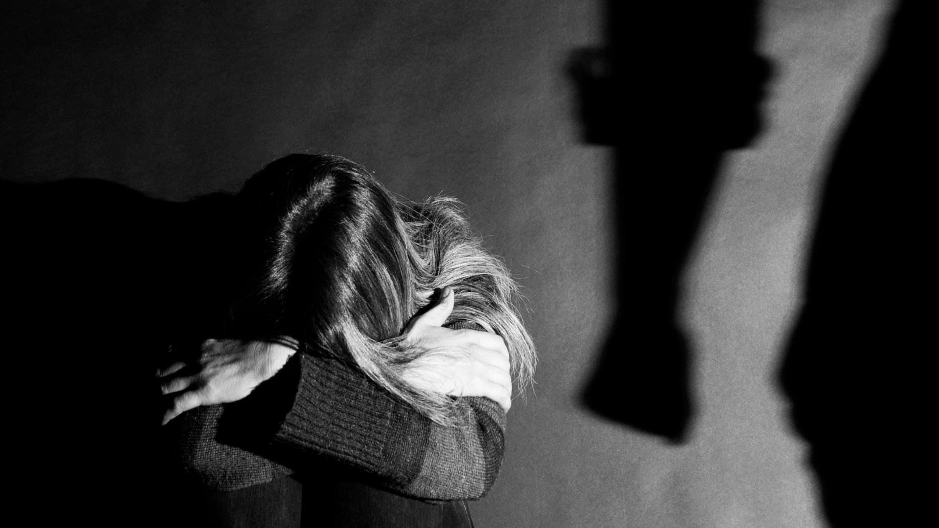 Young woman holding her head in her hands with shadow of someone's arm