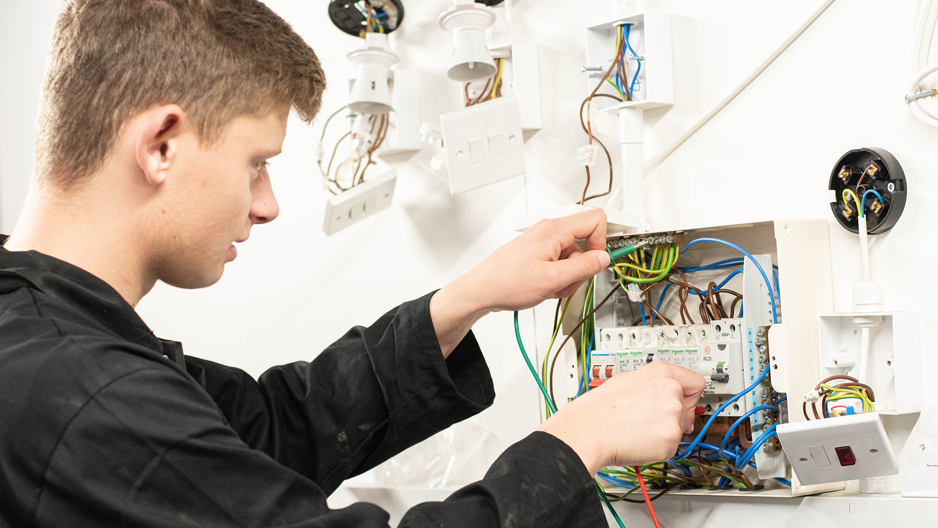 Man wearing hard hat and rubber gloves, fixing a circuit board.