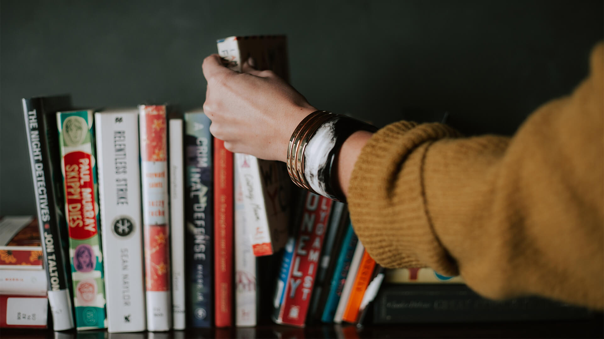 A row of books with a hand grabbing one.