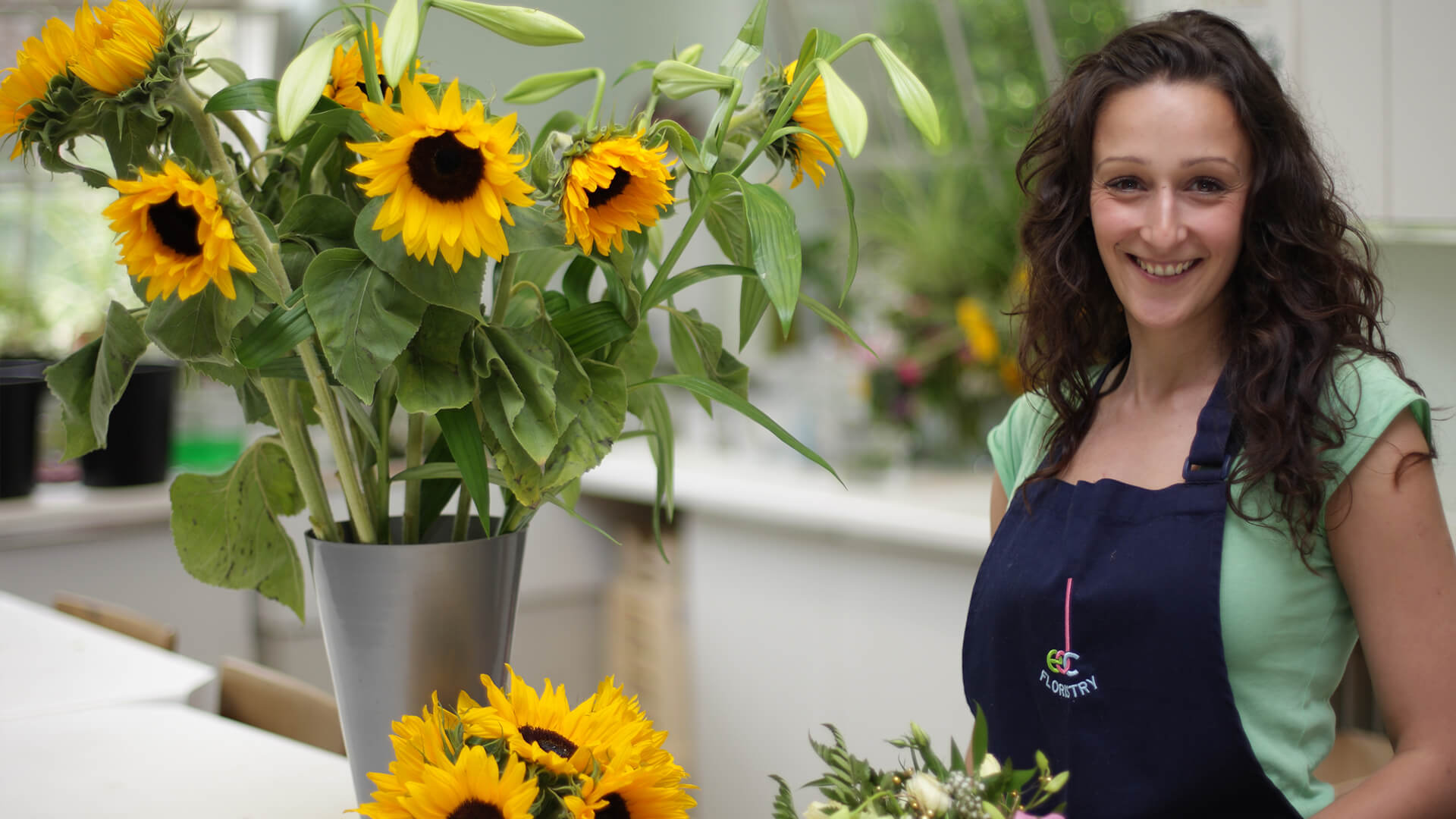 A woman smiling next to a bouquet of sunflowers.