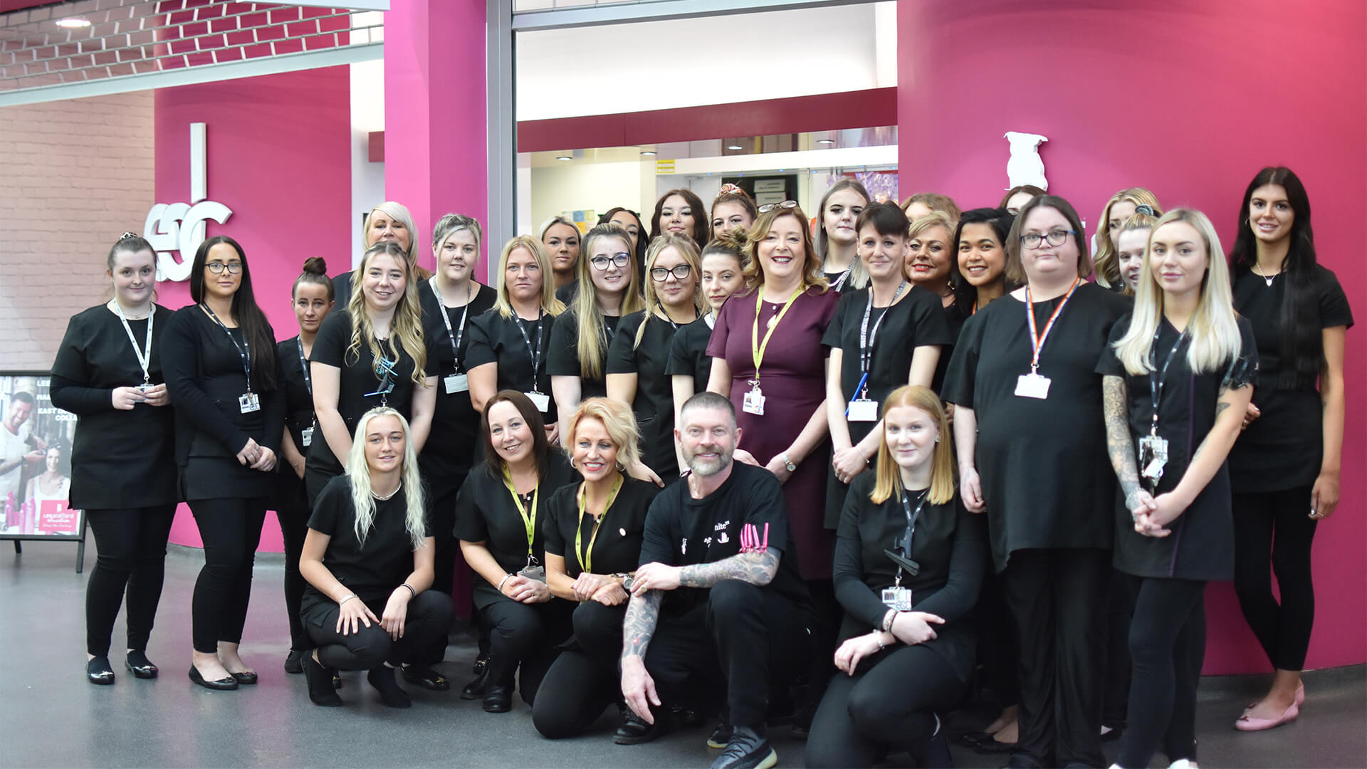 A group shot of students, staff and celebrity hair stylist, Lee Stafford, standing in front of the entrance of East Durham College's hair and beauty salon.