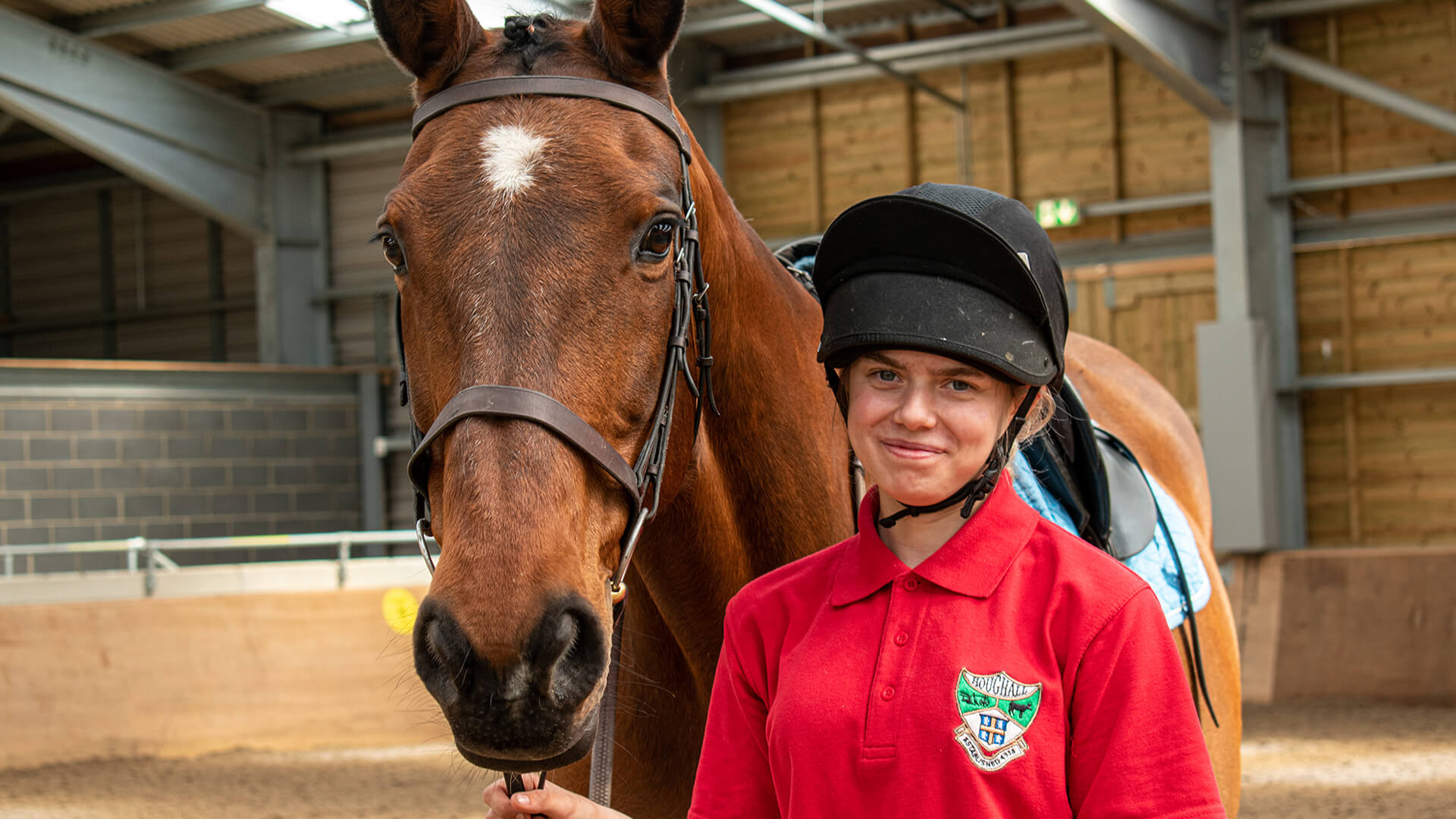 Young woman wearing equine gear whilst standing next to a brown and white horse in East Durham College's Equine centre.