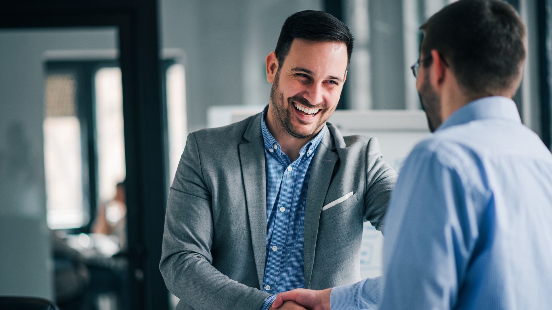 Man in a suit smiling and shaking hands with another man