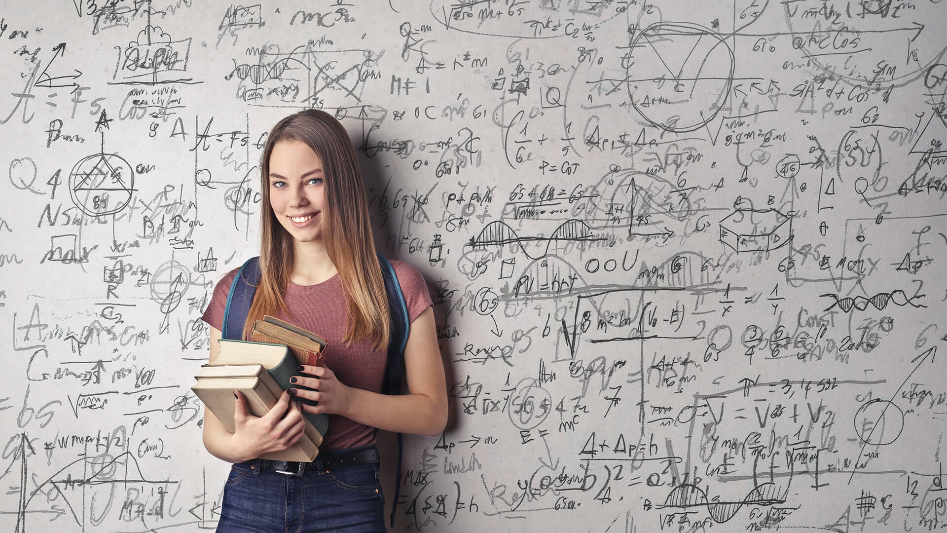 Students holding textbooks in front of a large whiteboard which has numerous of sums wrote on it.