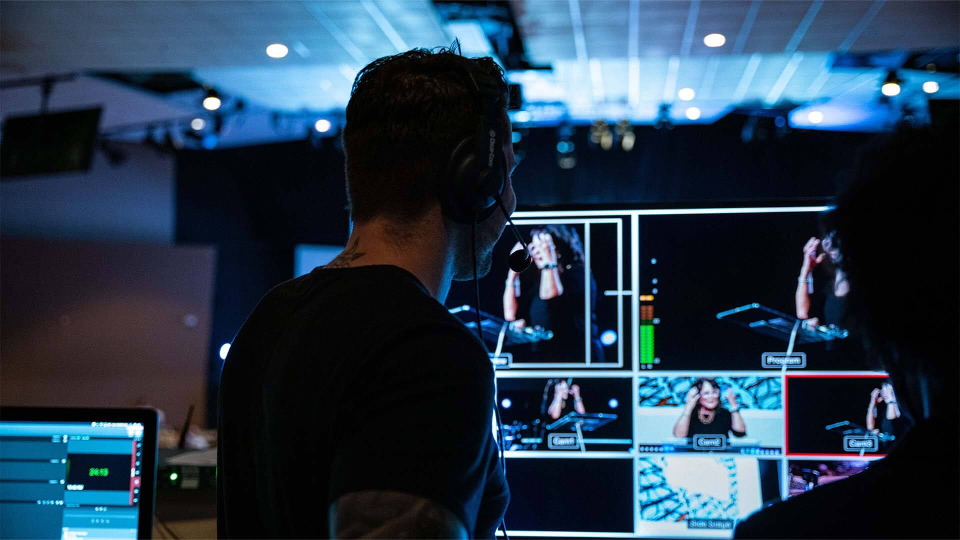 A young man looking at a computer screen which shows media footage being edited.