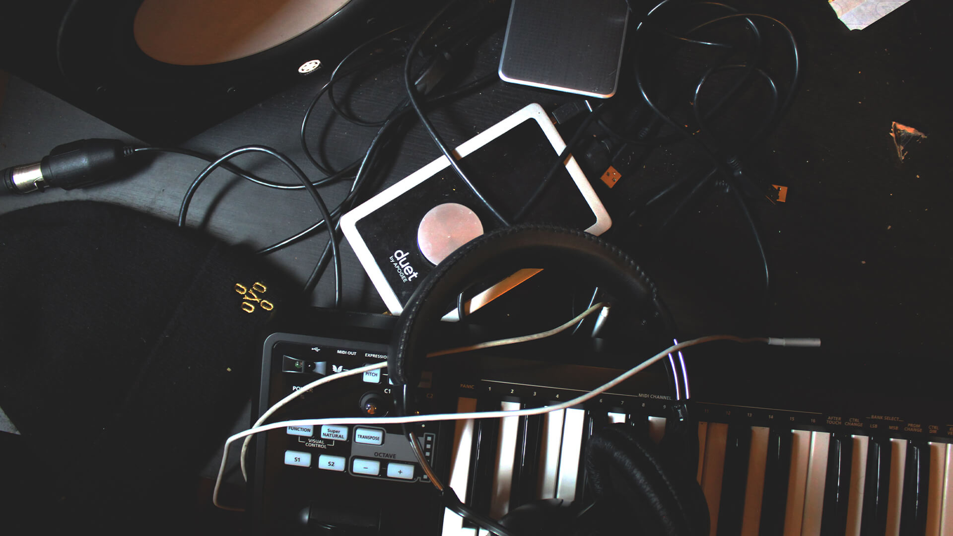 Pile of music gear like headphones, keyboard, wires and a smart tablet.