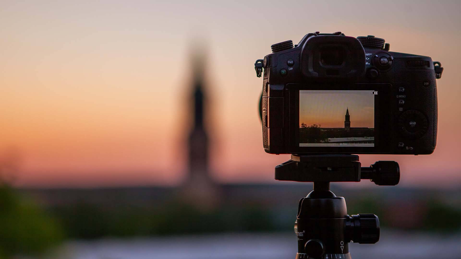 The back of a professional camera, with the display screen showing a sunset landscape.