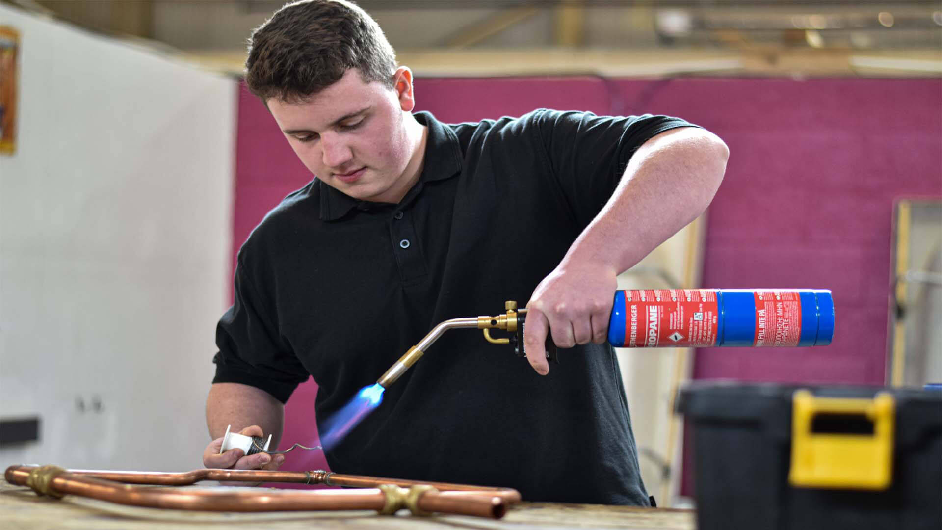 A man holding a blowtorch working on some copper pipes.