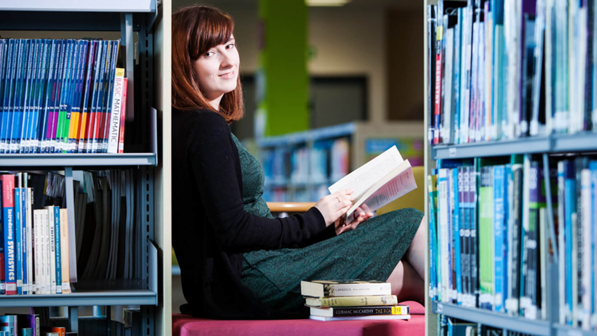 Young woman sat in the library reading a book.