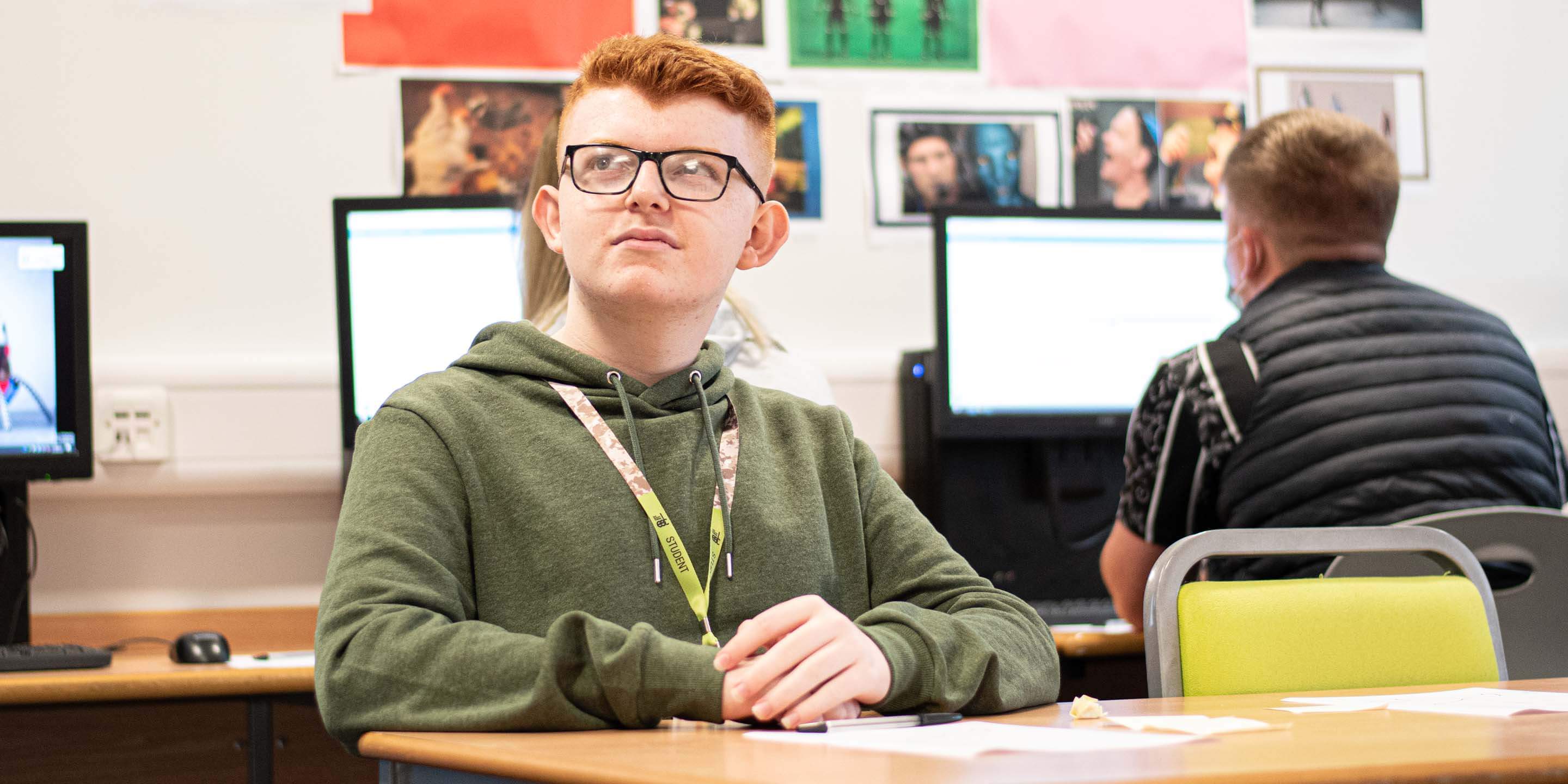 Young man in a classroom with computers behind him.