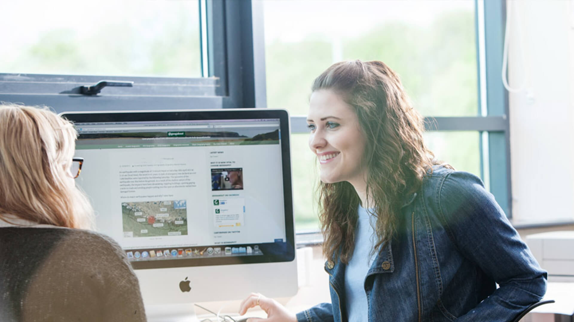 Two young women at a computer, having a conversation and smiling.