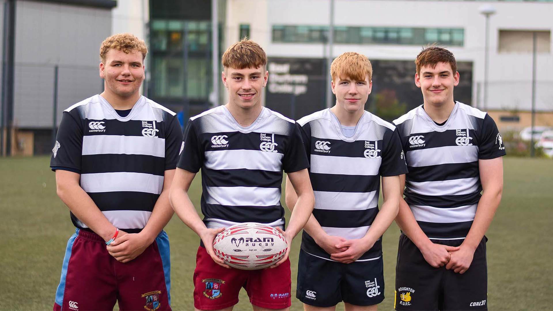 Four young men wearing East Durham College rugby uniforms and smiling on a pitch. One of the young men are holding a rugby ball.