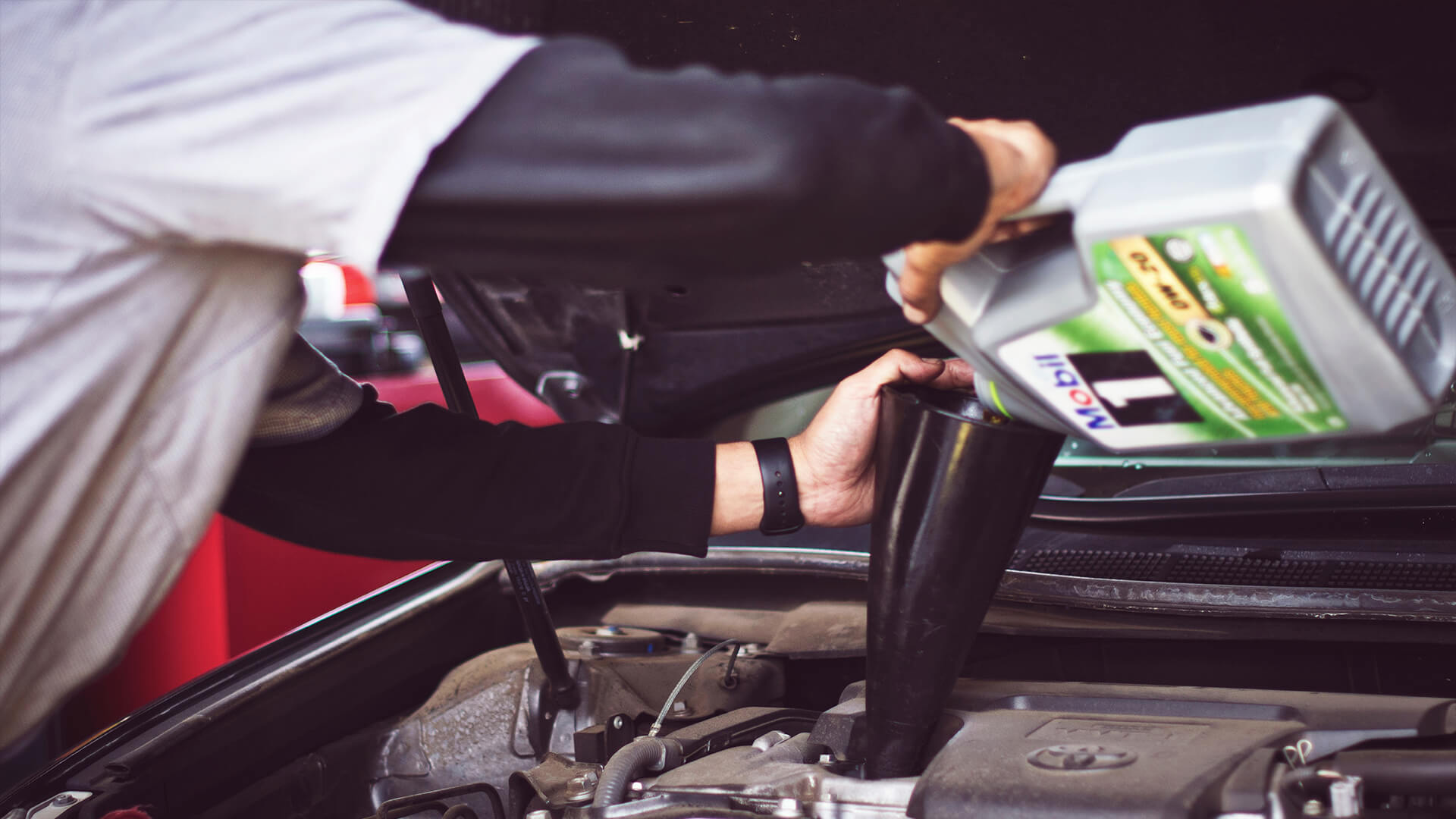 A person refilling oil into a car.