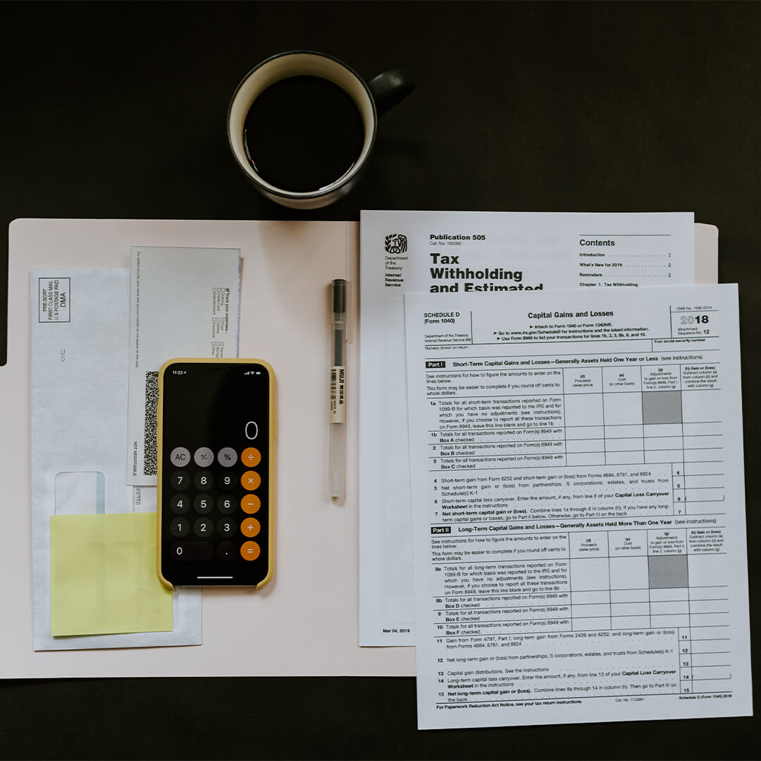 Tax paperwork in a file, pen, mug with coffee in it and a phone open on the calculator app.