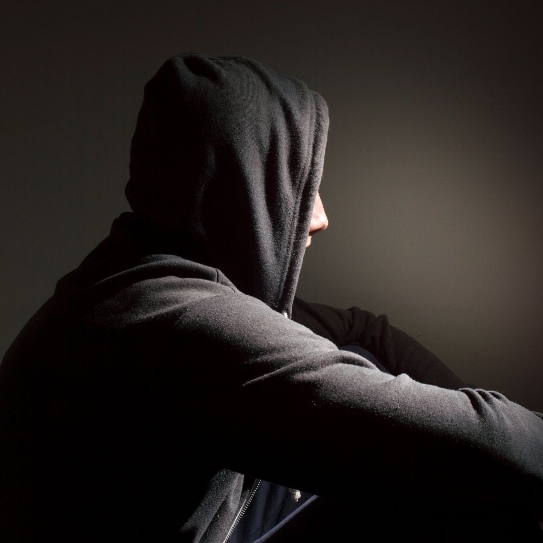 Teenager in black hoodie sitting and looking away from the camera