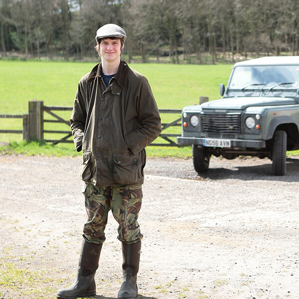 A young man in farmers gear standing by a field and a truck.