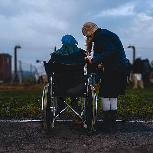 A woman caring for another person who is in a wheelchair in a park.