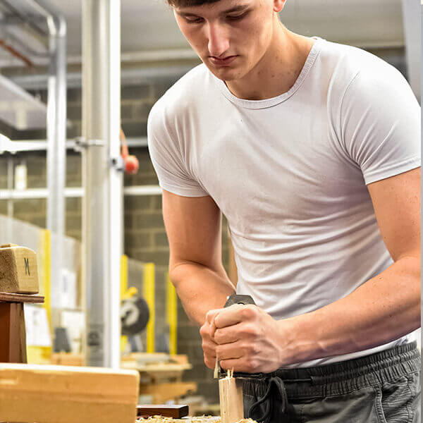 A young man working on some wood work on a work bench.