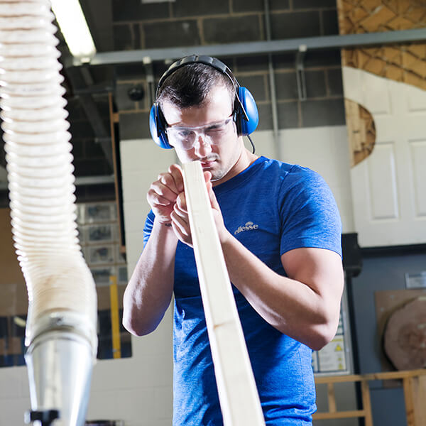 Young man wearing ear defenders holding a large piece of wood.