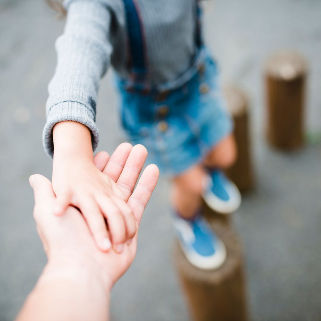 Child climbing on wooden stakes holding adult's hand