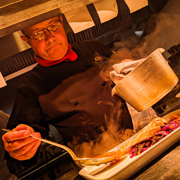 Chef holding a pot and spoon and dishing out food onto a plate.