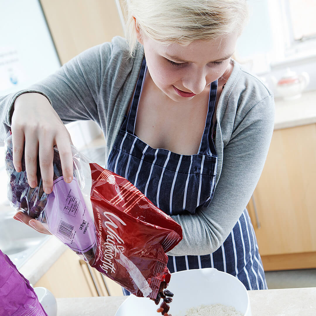 Young woman wearing an apron and pouring flour into a bowl.