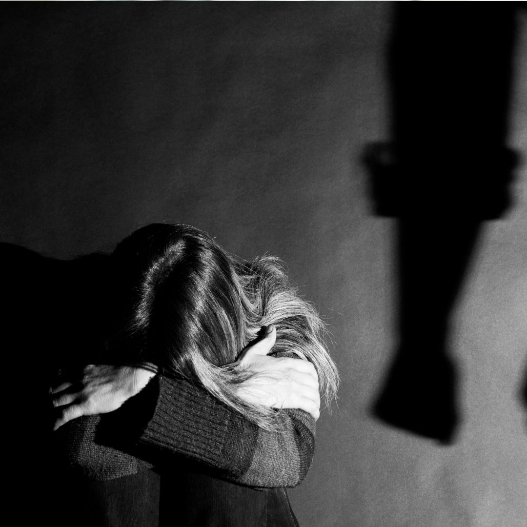 Young woman holding her head in her hands with shadow of someone's arm