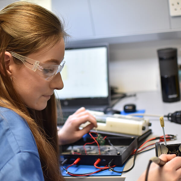 A young woman wearing safety goggles and using a soldering device.