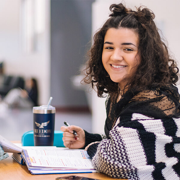 Young woman at a desk, with a pen in her hand and reading a textbook.