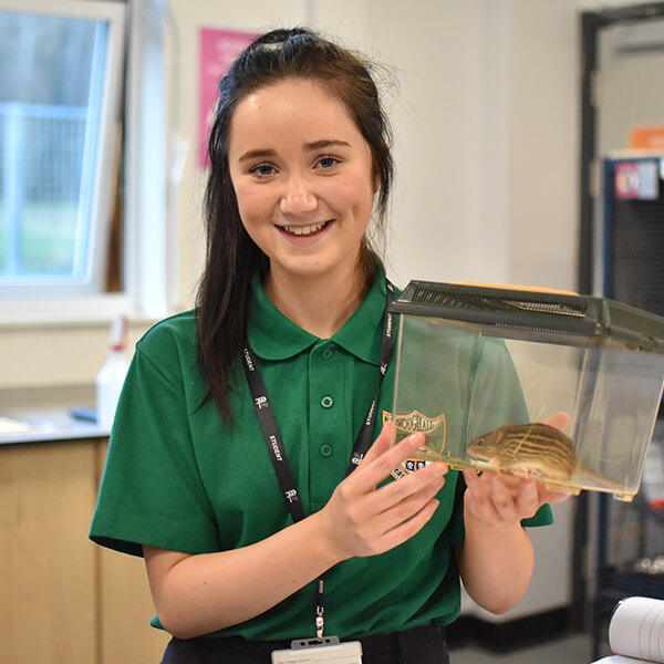 Young woman smiling whilst holding a clear plastic cage that has a zebra mouse in it.