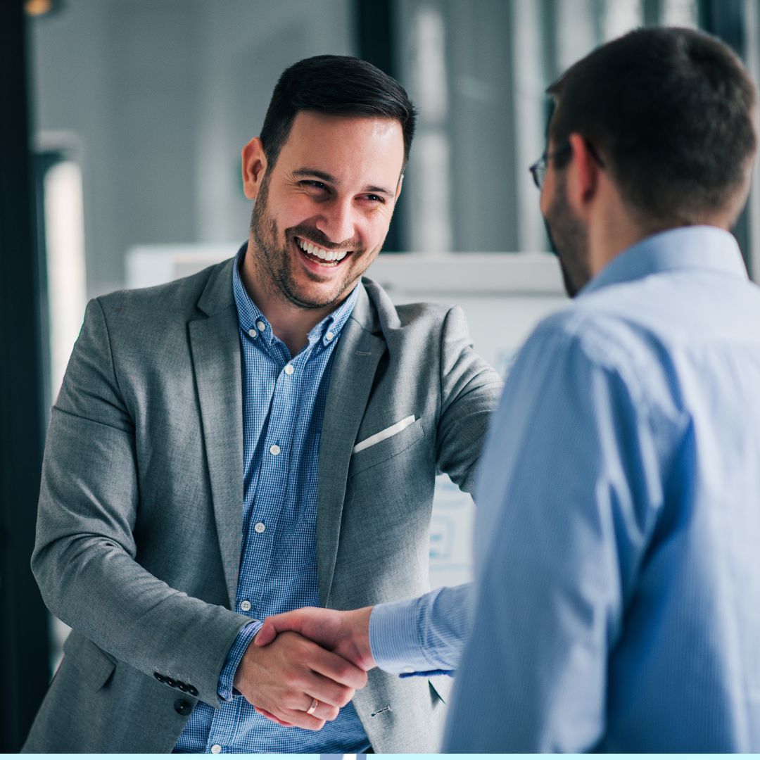 Man in a suit smiling and shaking hands with another man