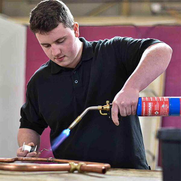 A young man using a blowtorch on copper pipes.