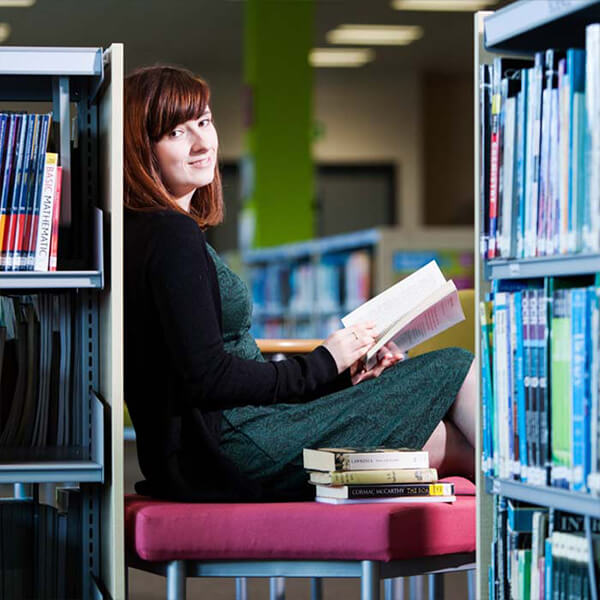 Young woman sat in the library reading a book.