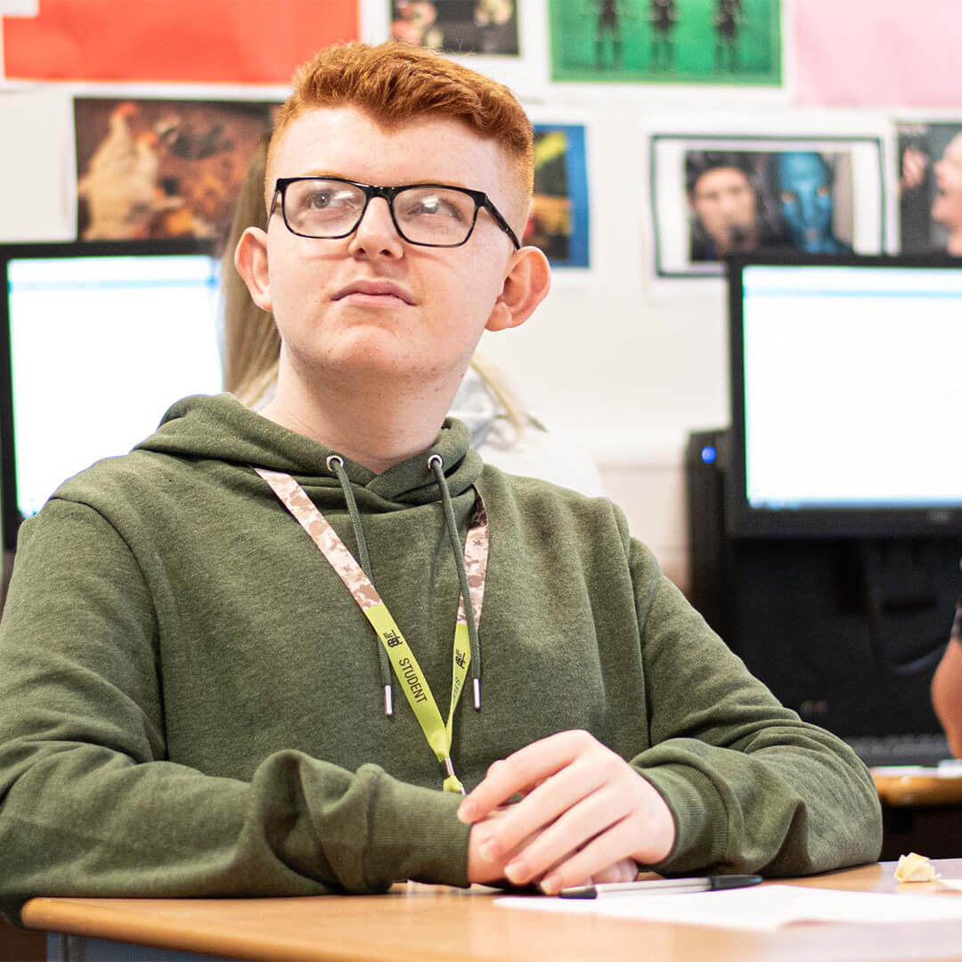 Young man in a classroom with computers behind him.