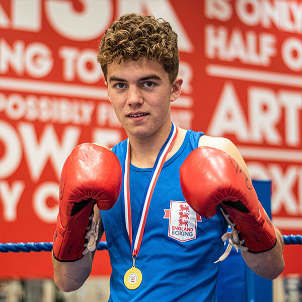 A young man wearing boxing gloves, holding both hands up in a boxing ring.