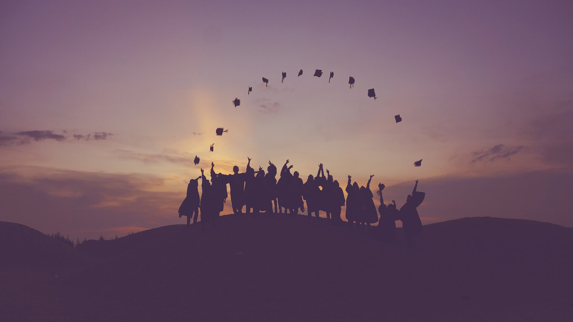 A group of students in silhouette throw mortar boards into the air