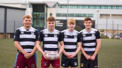 Four rugby students smiling at camera with a building behind them