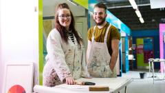 Two painting and decorating students in painting workshop pose with brushes and arms crossed