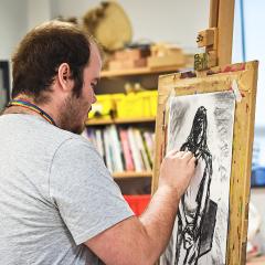 Art student completing charcoal drawing on an easel