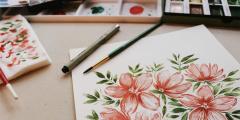 Watercolour painting of pink flowers and art supplies on a table