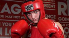 Boxer posing for camera with red boxing glovers held up and a re head guard on