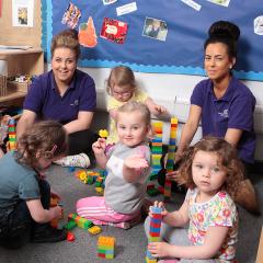 Childcare students playing with a small group of young children on carpet with building blocks