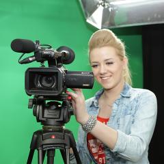 Smiling blonde girl looks into a video camera in front of greenscreen